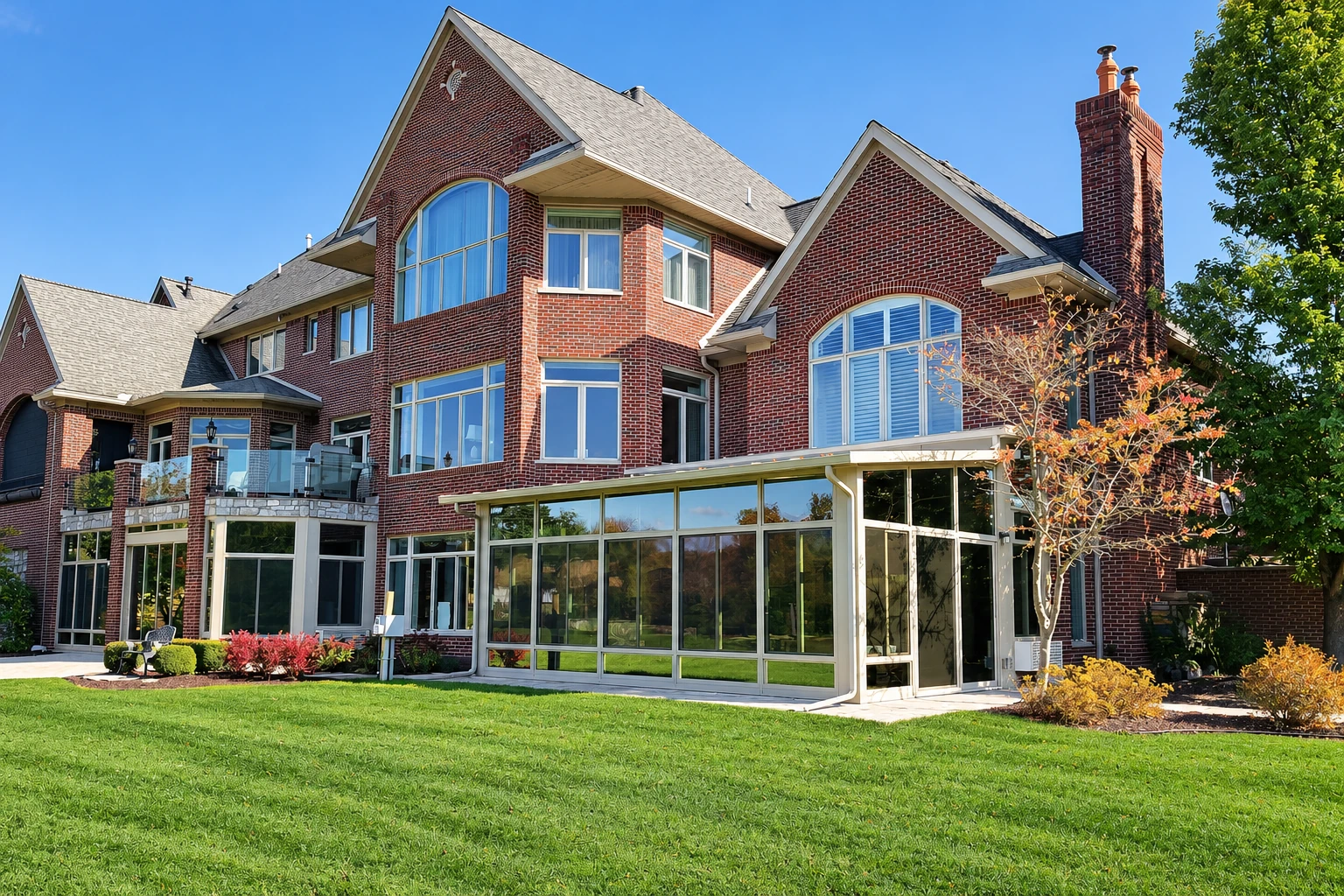Red-brick home with a large glass-walled all-season room extending onto a green lawn.