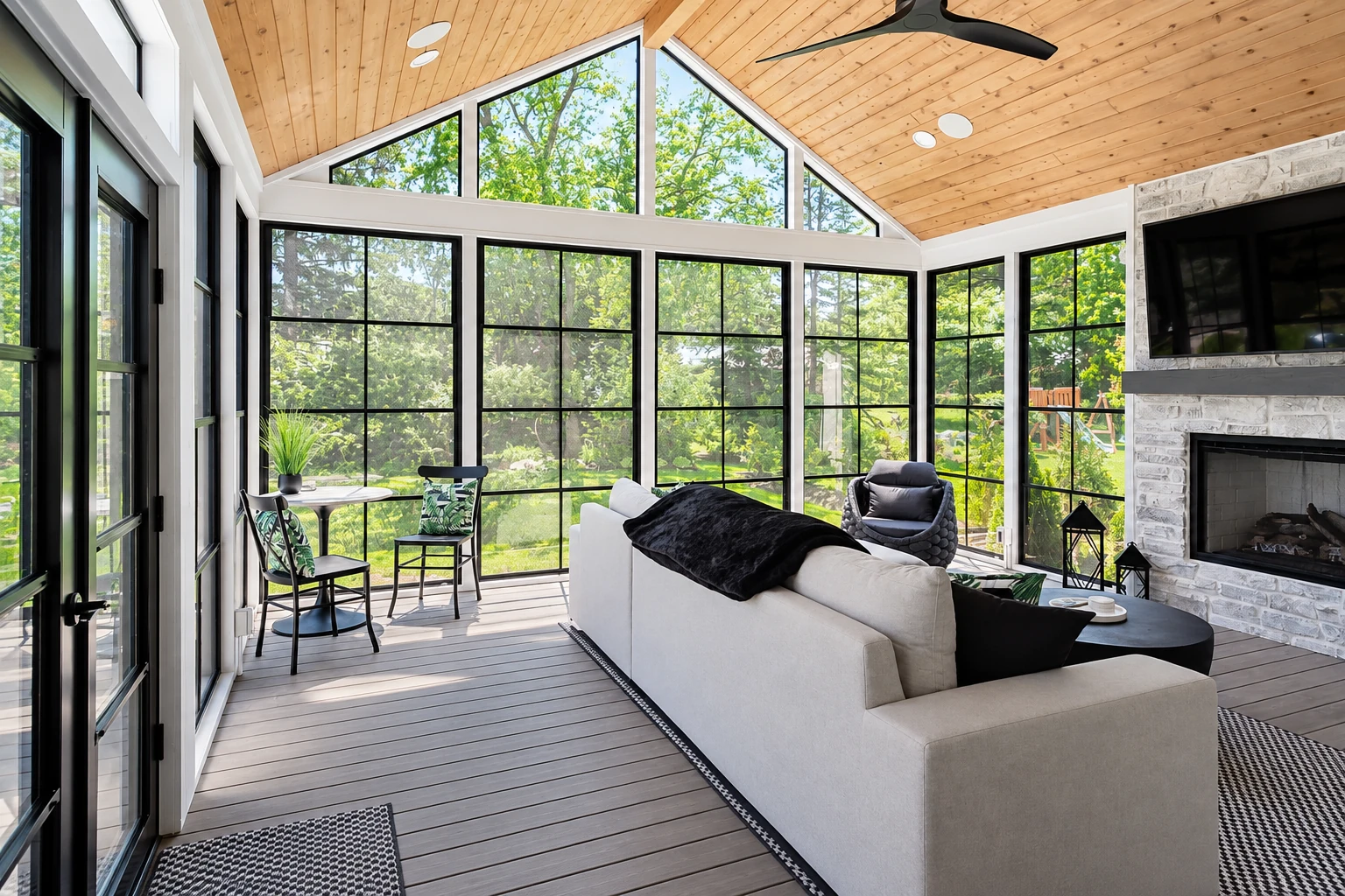 All-season sunroom with a peaked wood ceiling, expansive windows, a fireplace, and white seating.