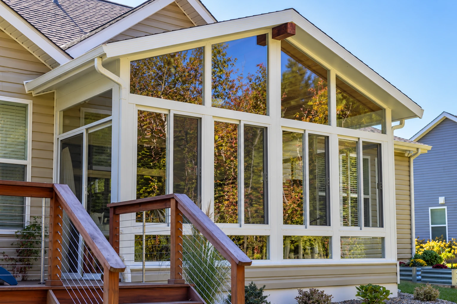 Custom sunroom with tall white-framed windows beneath a peaked roof, adjoining a wooden deck and stairs.