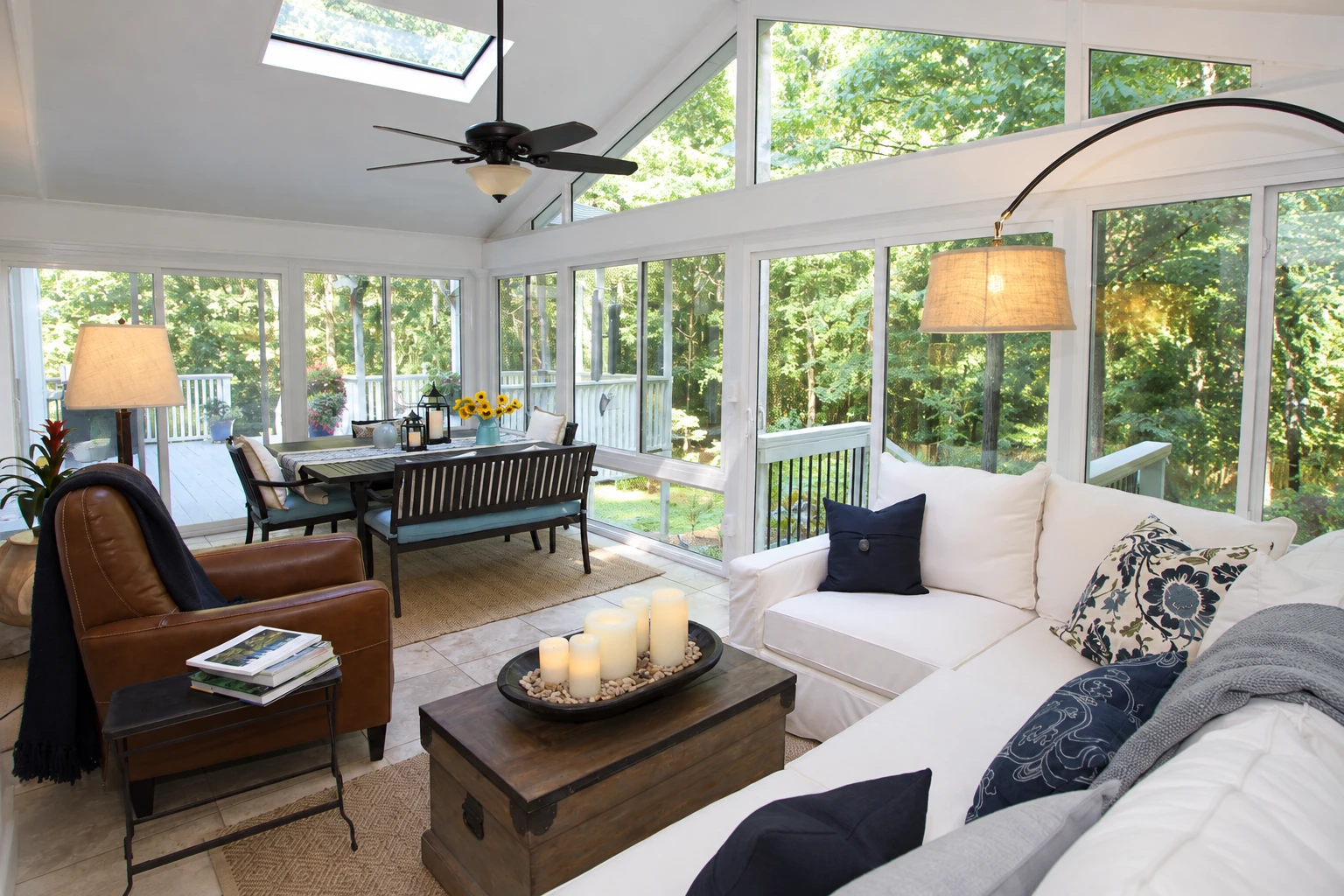 Bright enclosed sunroom with expansive windows, a skylight, white sofas, and a dining area.