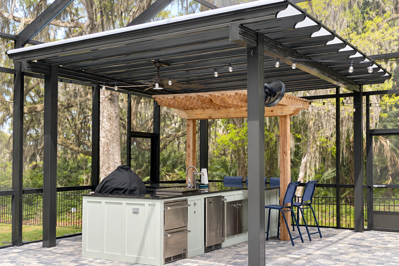 Covered outdoor kitchen beneath a dark metal patio cover, with ceiling fan, string lights and surrounding screens.