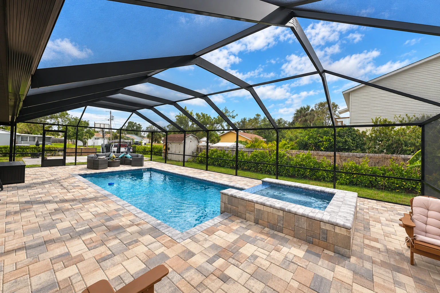 Screened patio enclosure surrounding a swimming pool, with a dark metal frame and paved deck.