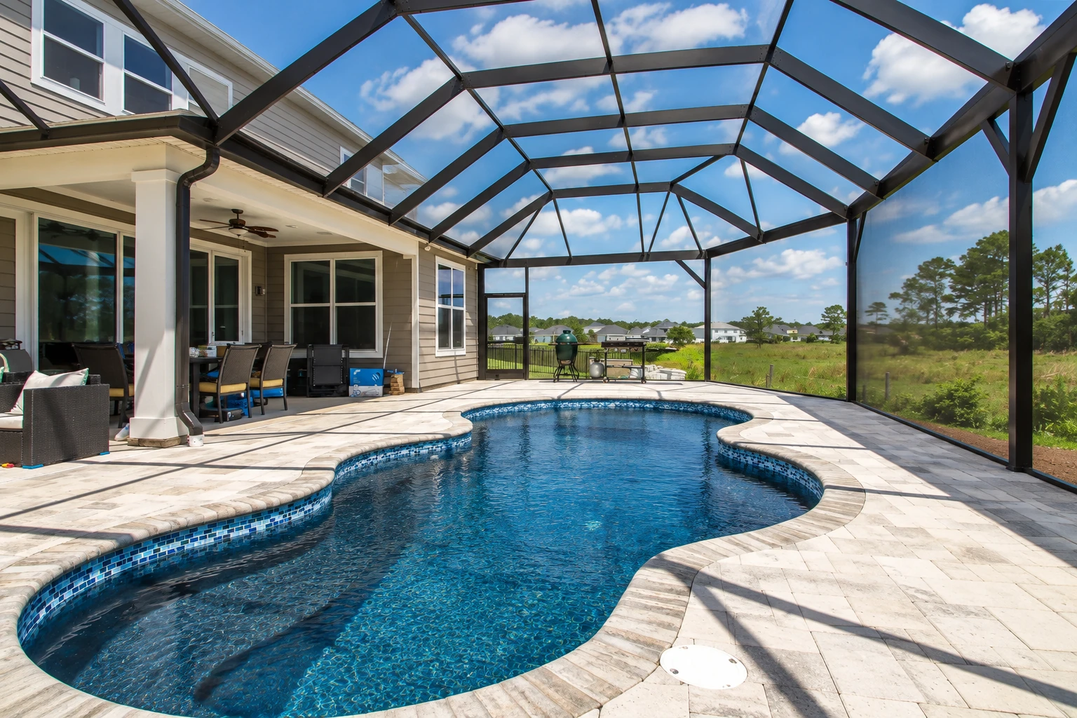 A screened pool enclosure with a dark metal frame, curved roof and paved deck around a blue swimming pool.