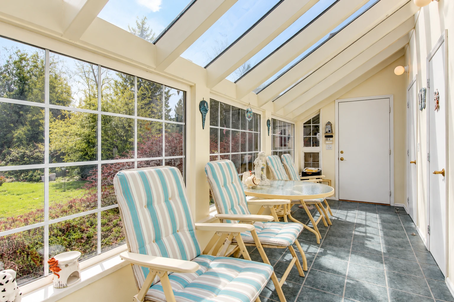 Sunroom addition with a glass-paneled sloped roof, tiled floor, and striped chairs beside expansive garden-facing windows.