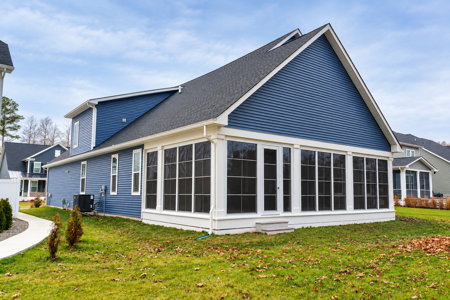 Blue-sided house with a newly built white-framed sunroom, tall windows, and a steep gabled roof.